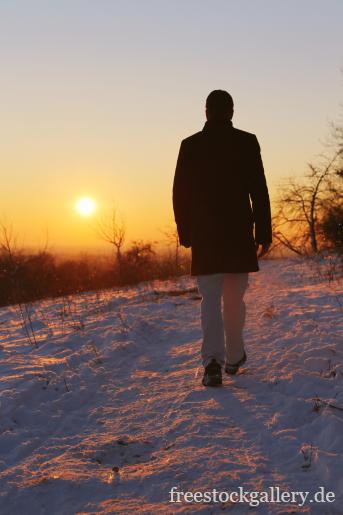 Mann spaziert im Schnee in den Sonnenuntergang