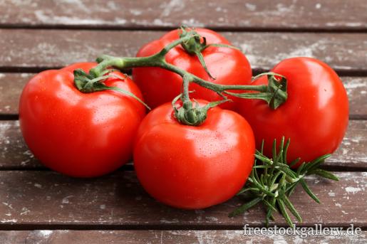 vier rote Tomaten auf einem Holztisch