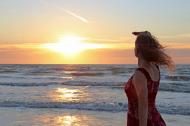 Frau schaut in den Sonnenuntergang am Meer - kostenloses Bild