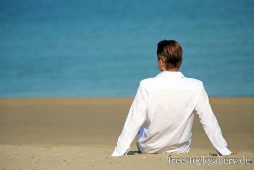 Mann sitzt am Strand und schaut auf Meer hinaus