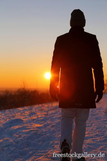 Mann geht im Schnee spazieren - Sonnenuntergang